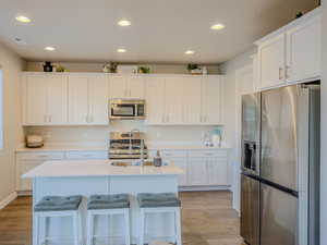 Kitchen featuring a kitchen island with sink, white cabinetry, and stainless steel appliances