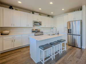 Kitchen featuring hardwood / wood-style floors, white cabinets, sink, an island with sink, and appliances with stainless steel finishes