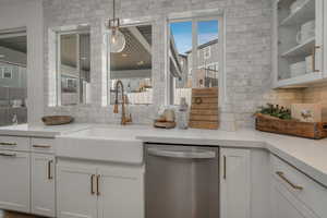 Kitchen with white cabinets, stainless steel dishwasher, hanging light fixtures, and sink