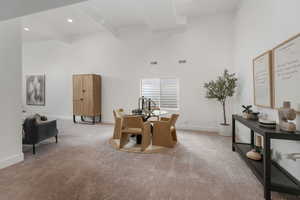 Dining space featuring light carpet, beamed ceiling, and a high ceiling