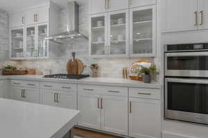 Kitchen featuring white cabinets, appliances with stainless steel finishes, tasteful backsplash, and wall chimney exhaust hood