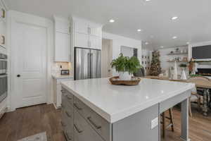 Kitchen featuring a kitchen island, tasteful backsplash, wood-type flooring, high quality fridge, and white cabinets