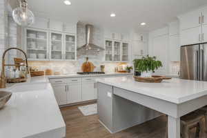 Kitchen featuring sink, wall chimney exhaust hood, hanging light fixtures, dark hardwood / wood-style flooring, and white cabinets