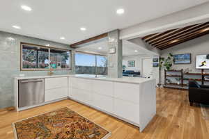 Kitchen featuring kitchen peninsula, stainless steel dishwasher, lofted ceiling with beams, light hardwood / wood-style flooring, and white cabinetry