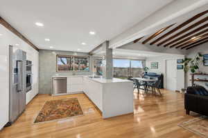 Kitchen with white cabinets, light hardwood / wood-style flooring, vaulted ceiling with beams, kitchen peninsula, and stainless steel appliances