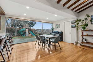 Dining space with vaulted ceiling with beams and light hardwood / wood-style flooring