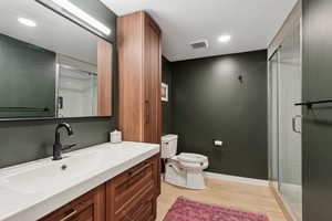 Bathroom featuring a shower with door, vanity, and toilet