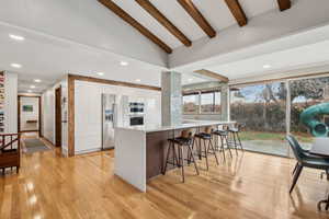 Kitchen featuring beam ceiling, stainless steel appliances, white cabinetry, and light hardwood / wood-style floors