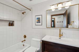 Full bathroom with vanity, toilet, tile walls, and tiled shower / bath combo