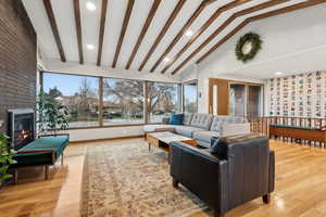 Living room with lofted ceiling with beams, light hardwood / wood-style floors, and a fireplace