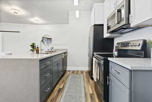 Kitchen featuring gray cabinetry, sink, appliances with stainless steel finishes, dark hardwood / wood-style flooring, and white cabinetry