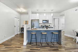 Kitchen with pendant lighting, a kitchen bar, white cabinets, appliances with stainless steel finishes, and dark hardwood / wood-style flooring