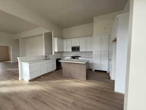 Kitchen with decorative backsplash, stainless steel appliances, sink, white cabinets, and a kitchen island.A pantry is concealed behind the cabinetry to the right of the stove.