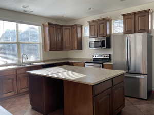 Kitchen with tile patterned floors, sink, a kitchen island, and stainless steel appliances