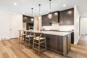 Kitchen with pendant lighting, wall chimney exhaust hood, light wood-type flooring, and sink