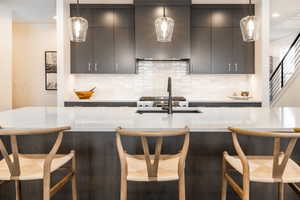 Kitchen with sink, wall chimney exhaust hood, a kitchen breakfast bar, pendant lighting, and decorative backsplash