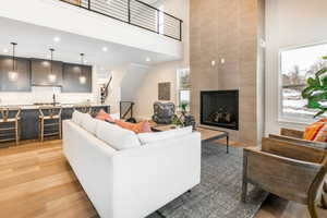 Living room with a tiled fireplace, a towering ceiling, and light hardwood / wood-style floors