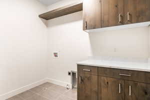 Clothes washing area featuring hookup for an electric dryer, hookup for a washing machine, cabinets, hookup for a gas dryer, and light tile patterned flooring