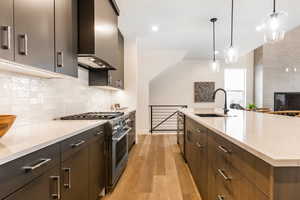 Kitchen with wall chimney range hood, hanging light fixtures, sink, light wood-type flooring, and appliances with stainless steel finishes