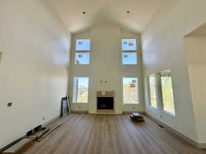 Unfurnished living room featuring wood finished floors, plenty of natural light, high vaulted ceiling, and a fireplace