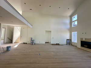 Unfurnished living room with light wood-style floors, high vaulted ceiling, and stairs