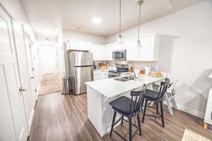 Kitchen featuring white cabinetry, stainless steel appliances, kitchen peninsula, wood-type flooring, and decorative light fixtures