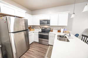 Kitchen featuring appliances with stainless steel finishes, sink, light hardwood / wood-style flooring, white cabinetry, and hanging light fixtures