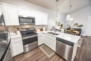 Kitchen with white cabinets, decorative light fixtures, stainless steel appliances, and kitchen peninsula