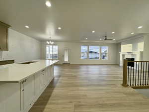 Kitchen with white cabinetry, hanging light fixtures, light hardwood / wood-style floors, a tray ceiling, and ceiling fan with notable chandelier