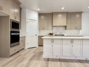 Kitchen featuring backsplash, light hardwood / wood-style floors, premium range hood, and appliances with stainless steel finishes