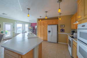 Kitchen with a center island, white appliances, sink, hanging light fixtures, and light tile patterned floors