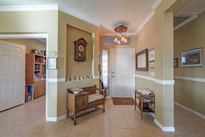 Tiled entrance foyer featuring crown molding, a textured ceiling, and a notable chandelier