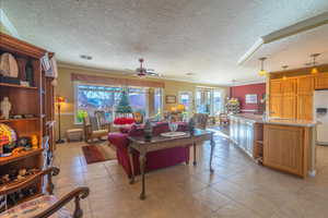 Great room with light tile patterned floors, a textured ceiling, ceiling fan, and ornamental molding