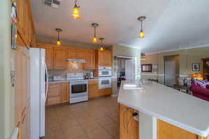 Kitchen featuring pendant lighting, white appliances, sink, and an island with sink