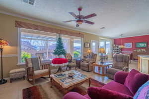 Living room with a textured ceiling, ceiling fan, light tile patterned flooring, and crown molding