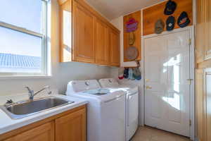 Laundry area featuring washer and clothes dryer, light tile patterned flooring, cabinets, and sink