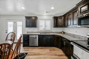 Kitchen with light stone countertops, dark brown cabinets, stainless steel appliances, sink, and light hardwood / wood-style flooring