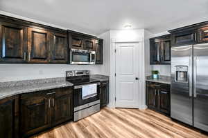 Kitchen featuring light stone counters, dark brown cabinetry, appliances with stainless steel finishes, and light hardwood / wood-style flooring