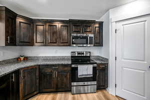 Kitchen with dark brown cabinets, dark stone countertops, stainless steel appliances, and light hardwood / wood-style flooring