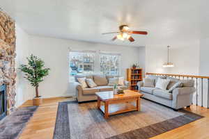 Living room with bamboo flooring, ceiling fan with notable chandelier, a textured ceiling, and a stone fireplace