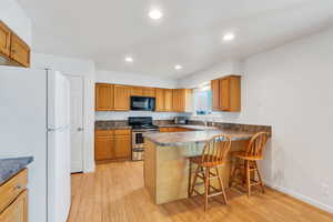 Kitchen featuring kitchen peninsula, white fridge, a breakfast bar area, stainless steel range with electric cooktop, and light wood-type flooring