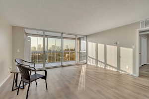 Empty room with floor to ceiling windows, light hardwood / wood-style floors, and a textured ceiling