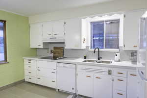 Kitchen featuring backsplash, white dishwasher, black electric stovetop, sink, and white cabinetry