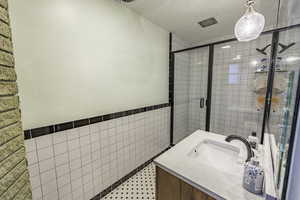 Bathroom featuring an enclosed shower, vanity, tile patterned floors, and tile walls