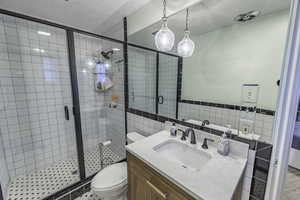 Bathroom featuring vanity, toilet, a shower with shower door, and tile walls