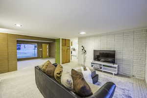 Carpeted living room featuring brick wall