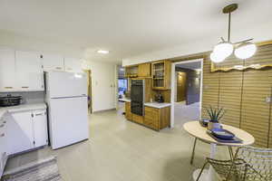 Kitchen with white cabinets, hanging light fixtures, light tile patterned floors, white fridge, and brick wall