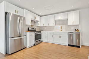 Kitchen with decorative backsplash, light wood-type flooring, stainless steel appliances, sink, and white cabinets