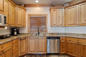 Kitchen with light stone counters, stainless steel dishwasher, and sink