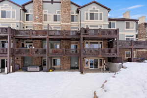 Rear of property. Back Patio to Condo. Snow covered property with a hot tub